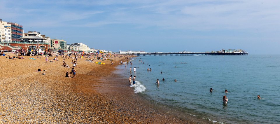 Brighton beach with many people swimming and sunbathing; pier in the background.