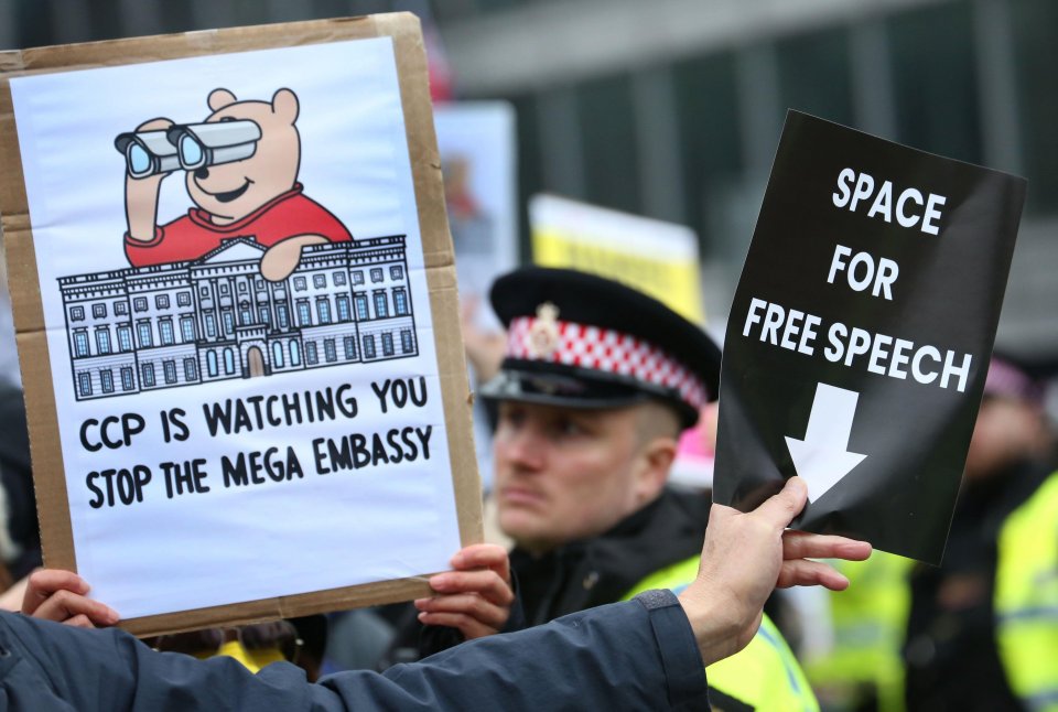 Protester holding signs that read "Space for Free Speech" and "CCP is watching you. Stop the mega embassy."