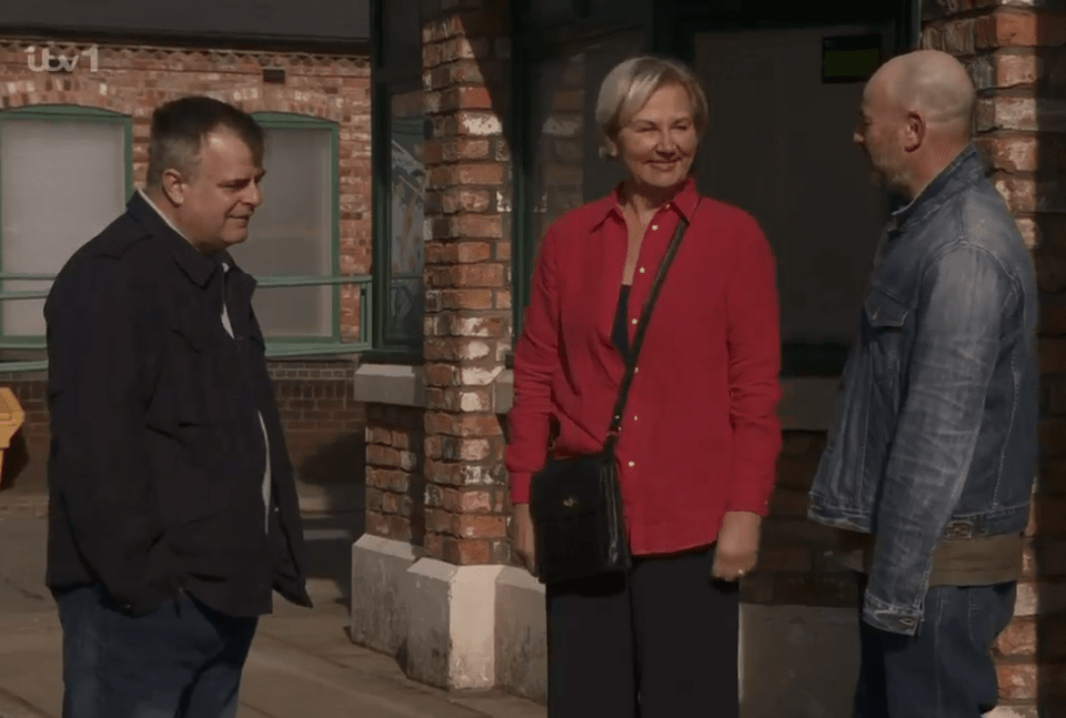 Three people talking outside a brick building.