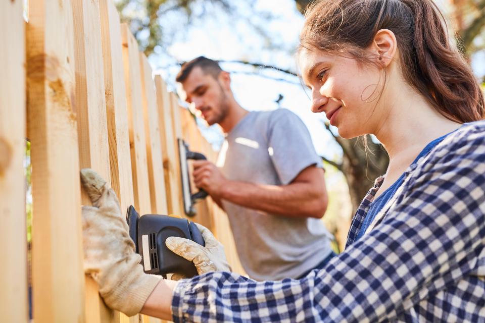 Young couple sanding a wooden fence.