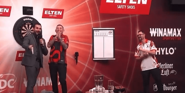 Three darts players on stage at a tournament.