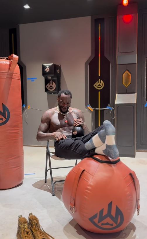 Deontay Wilder in his gym, sitting and holding a small punching bag.