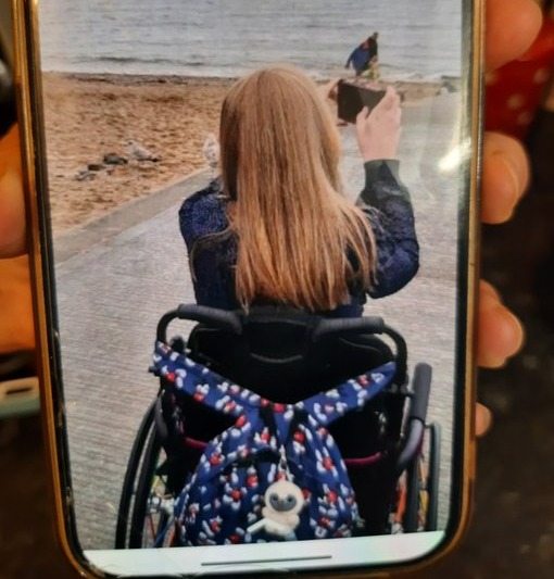 Person in wheelchair taking a photo of a beach and pier.