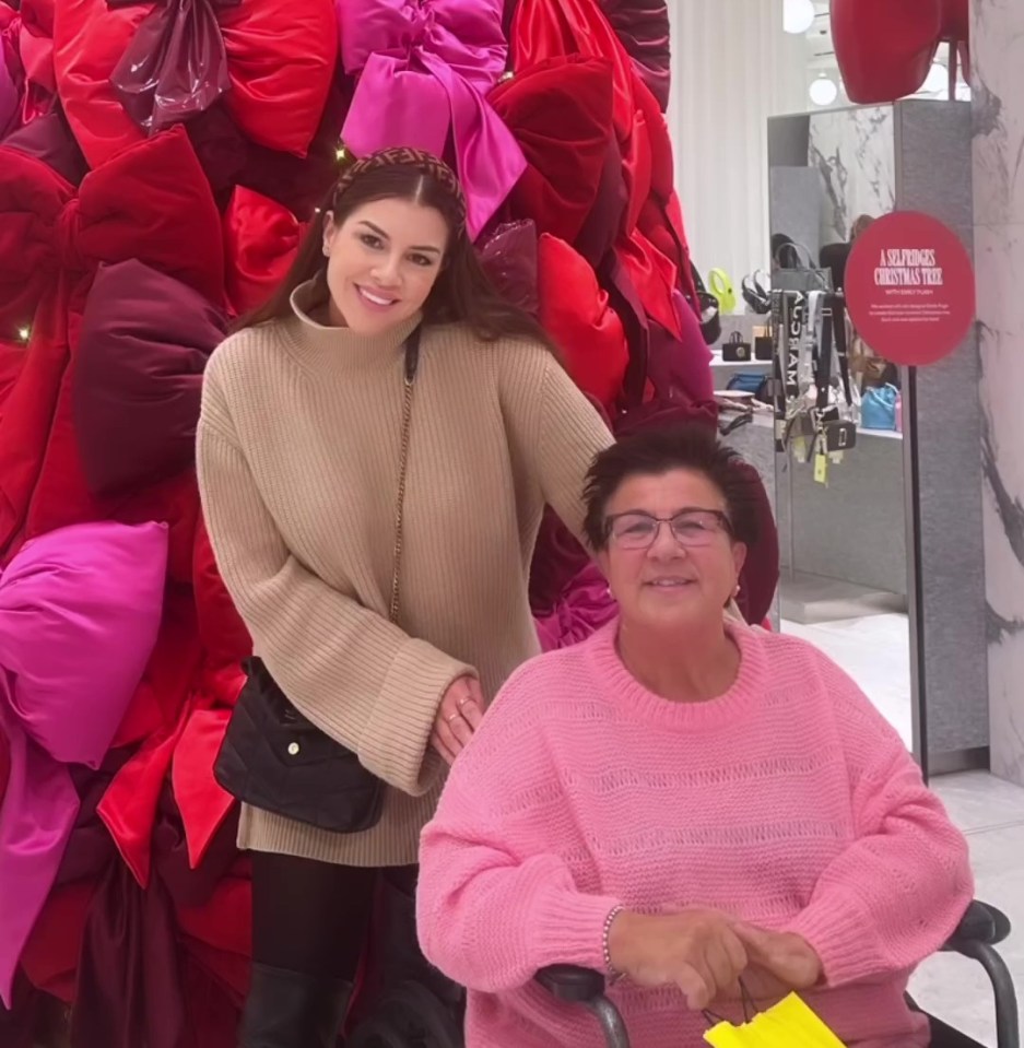 Two women posing in front of a large Christmas tree made of bows.