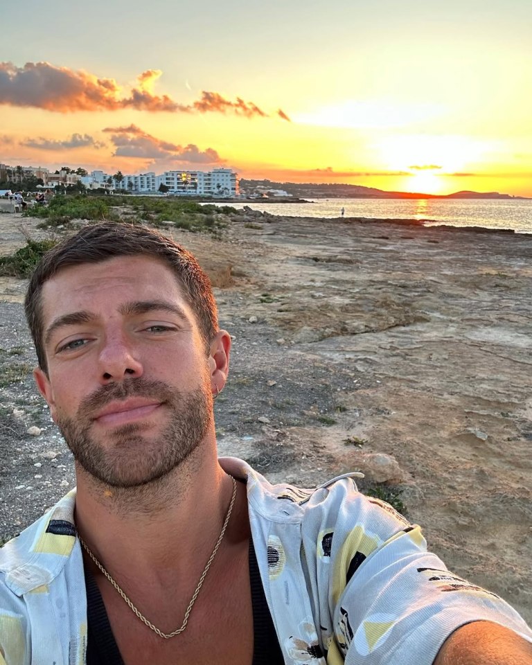 Man in patterned shirt at sunset by the ocean.