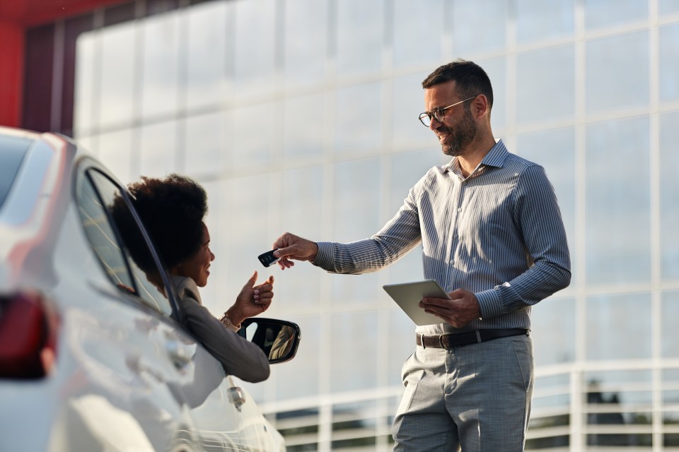 Happy salesman giving his African American female customer new keys of a car on the street.