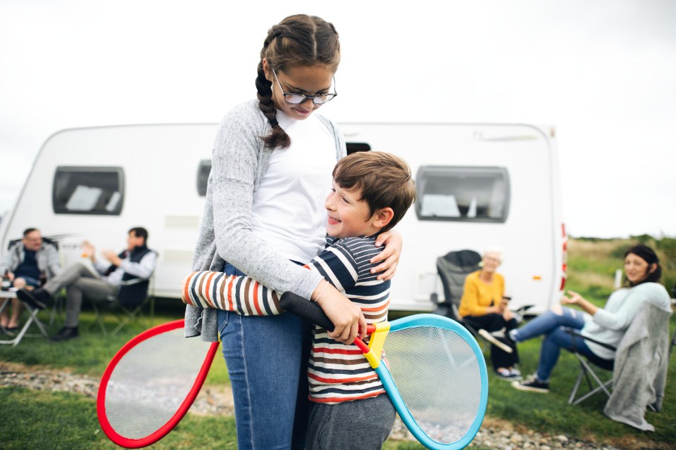 Brother and sister hugging while holding rackets outdoors near a campervan.