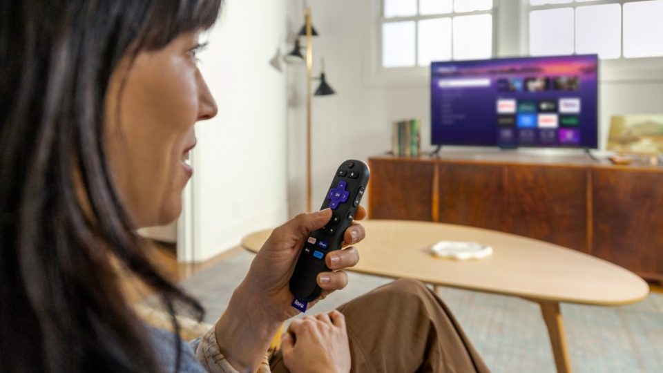 Person using Roku remote to navigate streaming service on TV.