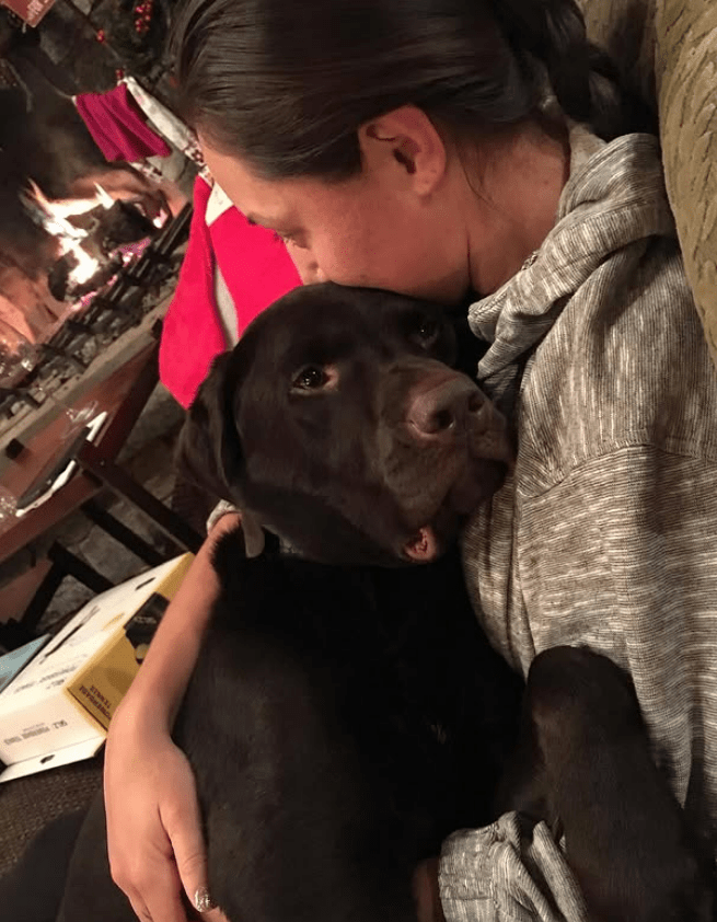 Woman hugging her chocolate Labrador Retriever.