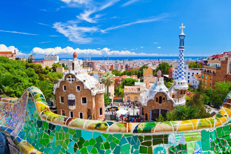 View of Parc Güell in Barcelona, Spain, showing the main entrance and the Barcelona skyline.