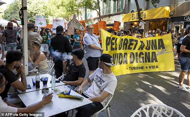 Tourists watch in Mallorca as demonstrators hold a banner reading 'For the right to a decent life'