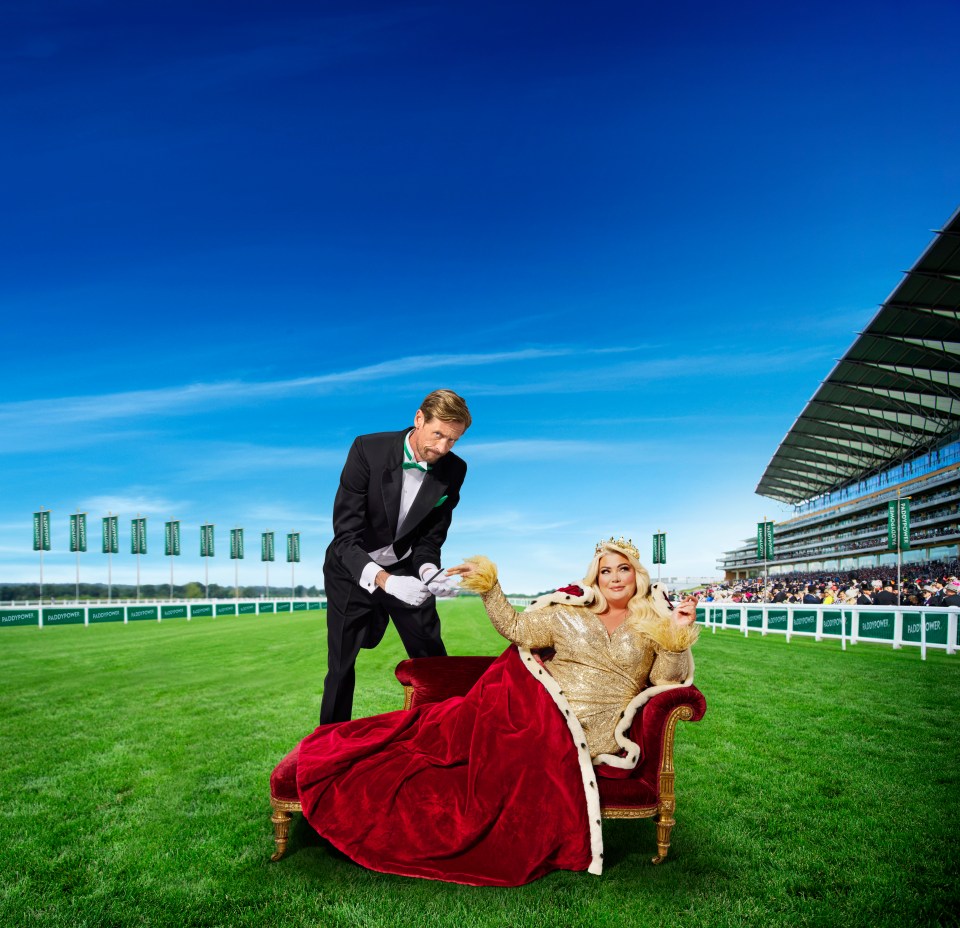 A woman in a queen's robe sits on a chaise lounge on a racecourse as a man in a tuxedo attends to her.
