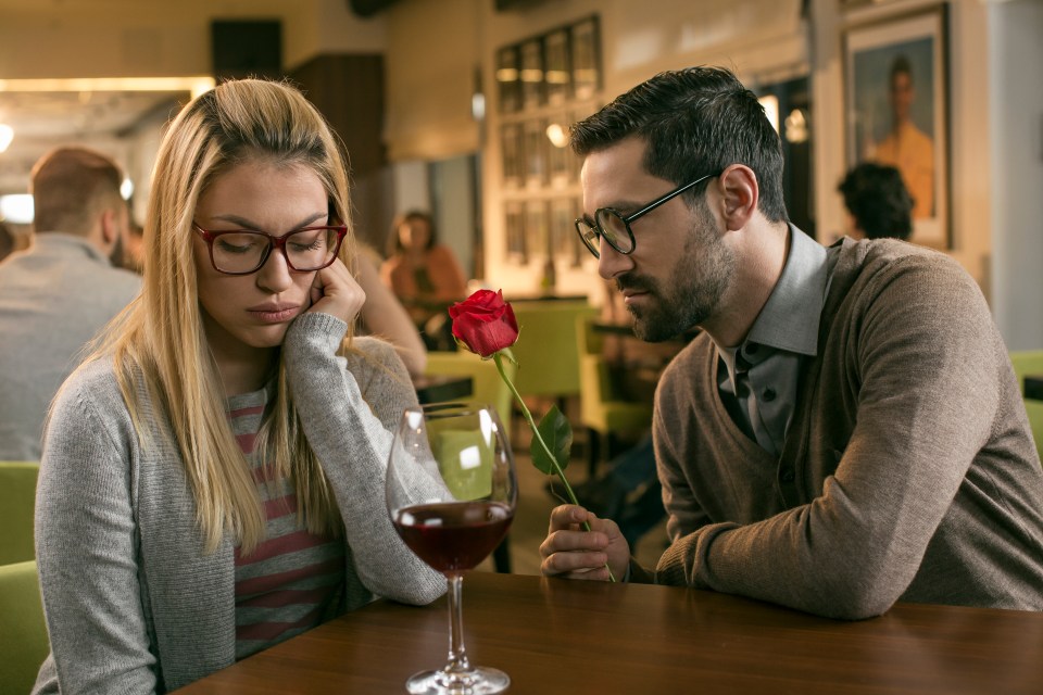 A man offering a red rose to a sad woman in a bar.
