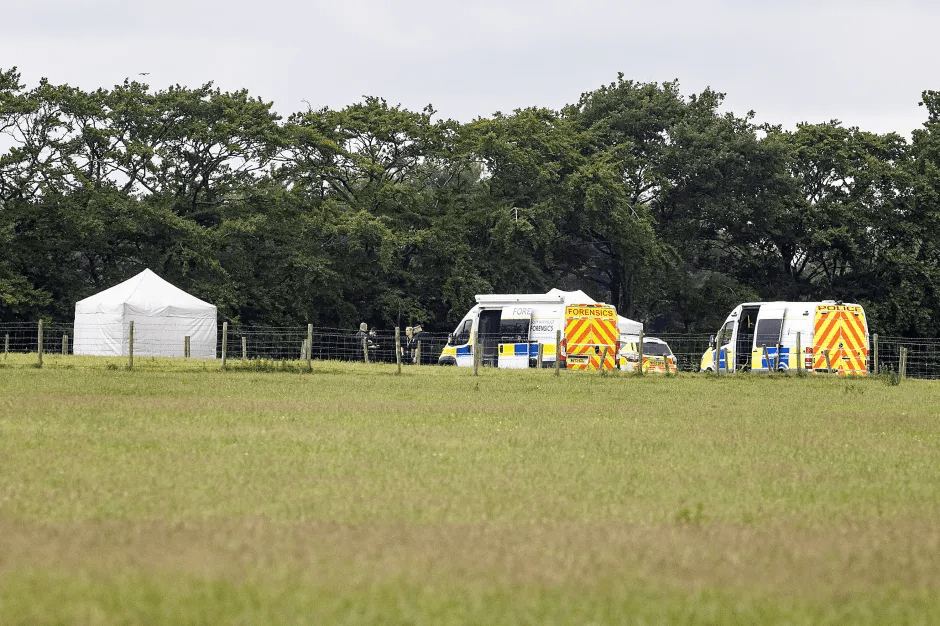Crime scene with police vehicles and a tent in a field.