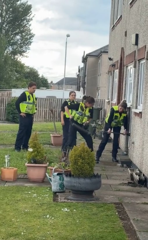 Police officers struggling to break down a door.