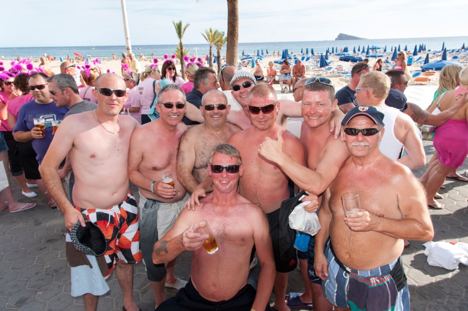 Group of shirtless British men drinking on a beach in Benidorm.