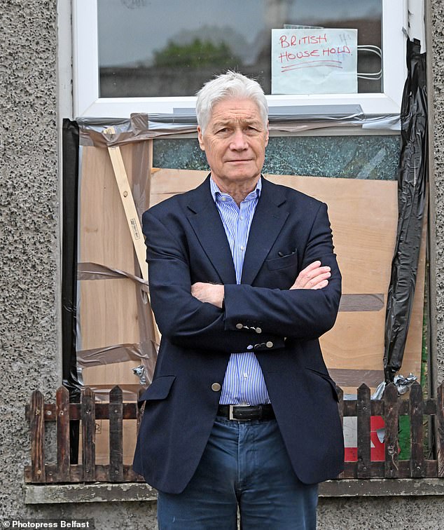 Richard Kay stands in front of a boarded up house that has a sign in the window reading: 'British Household'