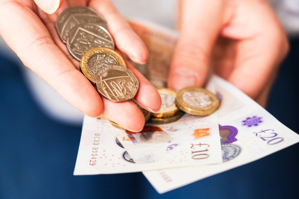 Hands holding UK coins and banknotes.