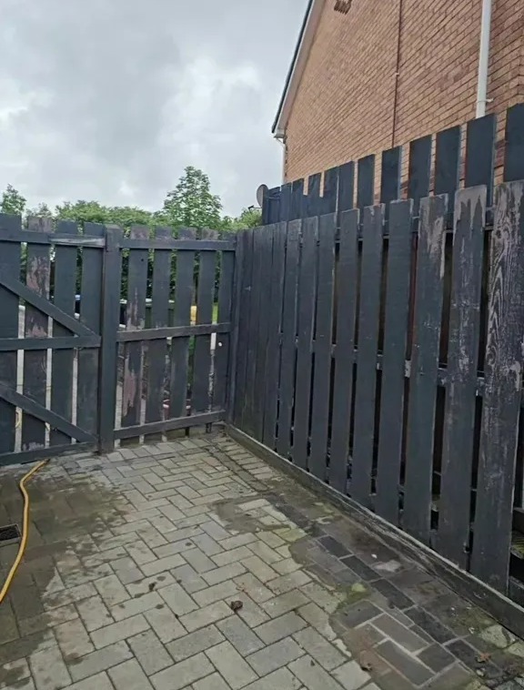 A newly installed dark gray fence and gate next to a brick house.