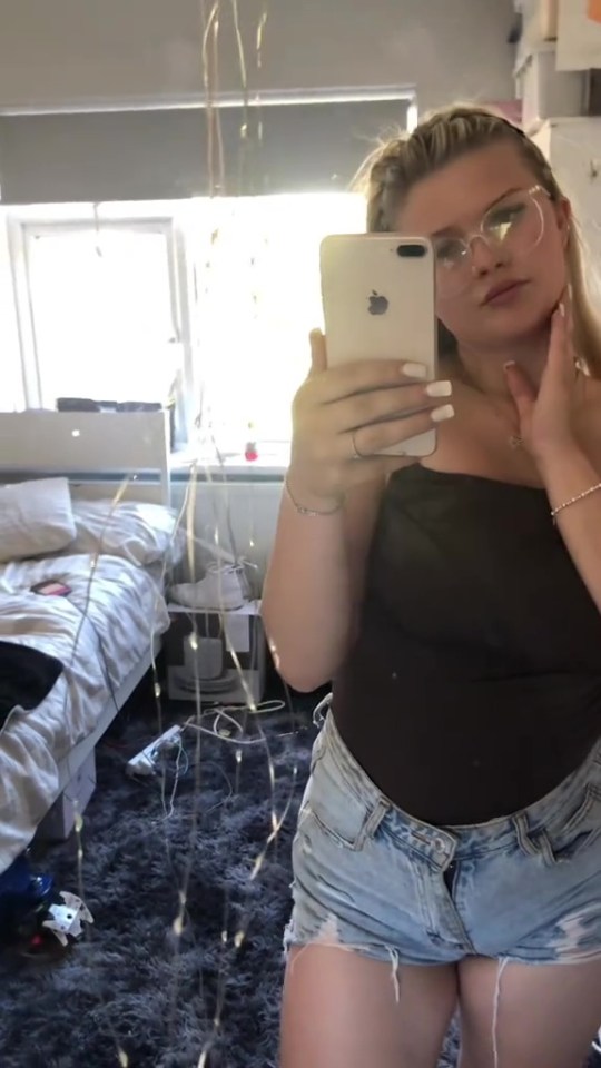 A young woman takes a selfie in her bedroom.