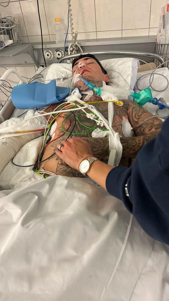 A tattooed man lying in a hospital bed hooked up to medical equipment.