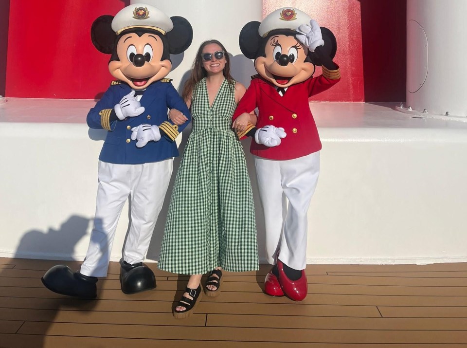 Woman posing with Mickey and Minnie Mouse in Captain's uniforms on a Disney cruise ship.