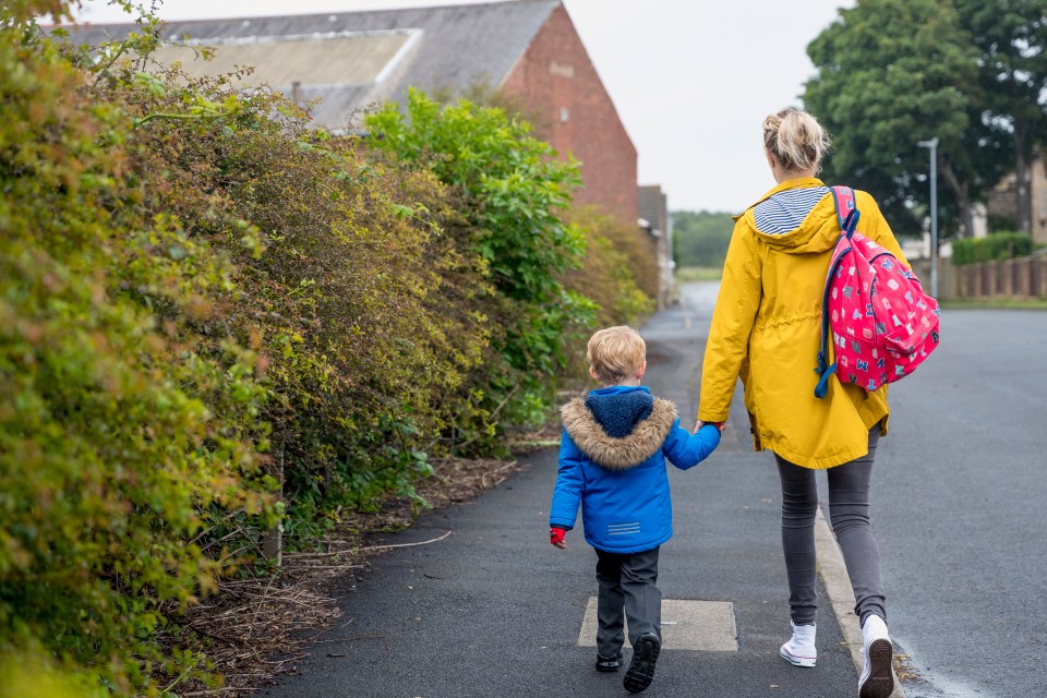 A mother and son holding hands walk to school.
