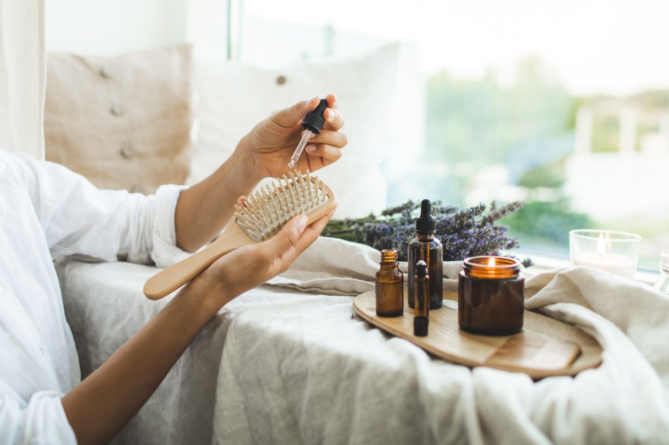 Woman applying lavender oil to a wooden hairbrush.
