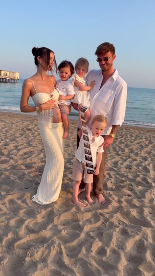 Family on beach announcing pregnancy with ultrasound photo.