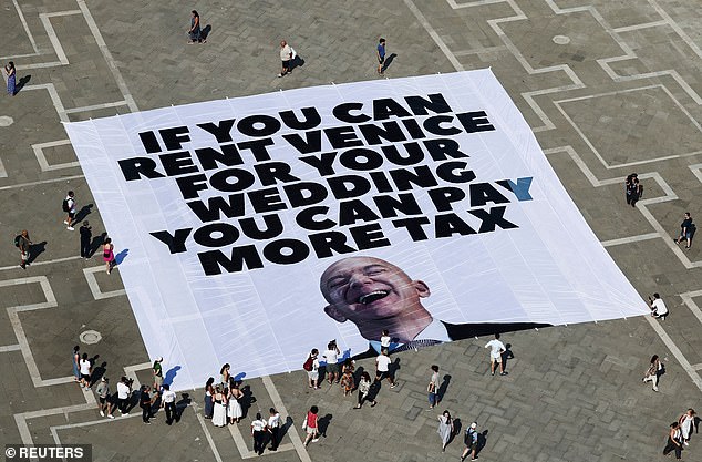 Amazon boss Jeff Bezos and bride to be Lauren Sanchez 's have been forced to change one of the venues for their £36million Venice wedding because of 'rising global tensions' it was claimed today. Pictured: A large banner against Amazon founder Jeff Bezos lies on the ground