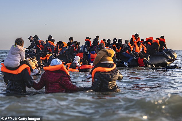 Migrants in the channel wading into water with children on their shoulders attempting to get on an inflatable boat