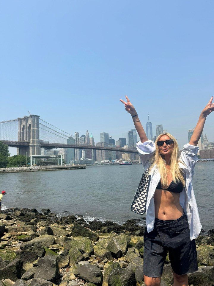 Woman making peace sign in front of the Brooklyn Bridge and New York City skyline.