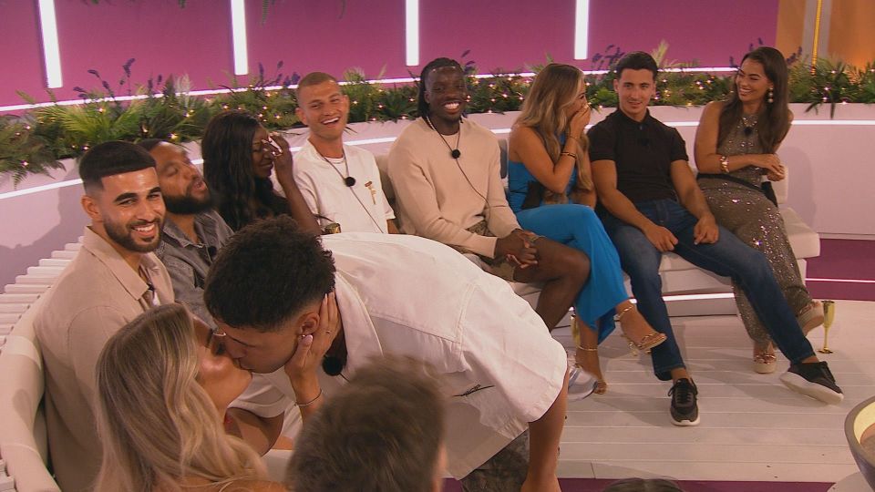 A couple kissing on Love Island, surrounded by other contestants.