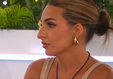 Woman with brown hair in a bun looking thoughtfully to the side.