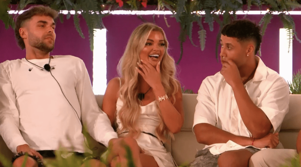 Screenshot of three people sitting on a couch; a woman is laughing, while a man on either side of her looks pensive.