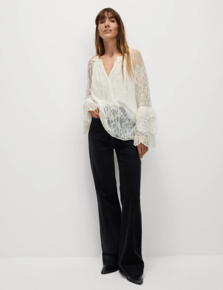 Woman wearing a white lace blouse and black flared jeans.
