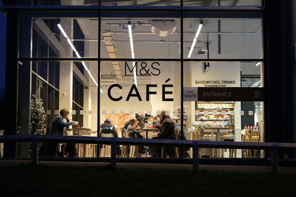 People dining at a brightly lit M&S cafe at night.