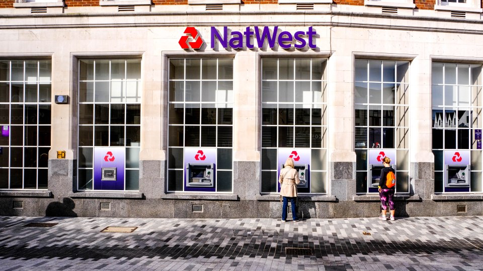 Two people using ATMs outside a NatWest bank.