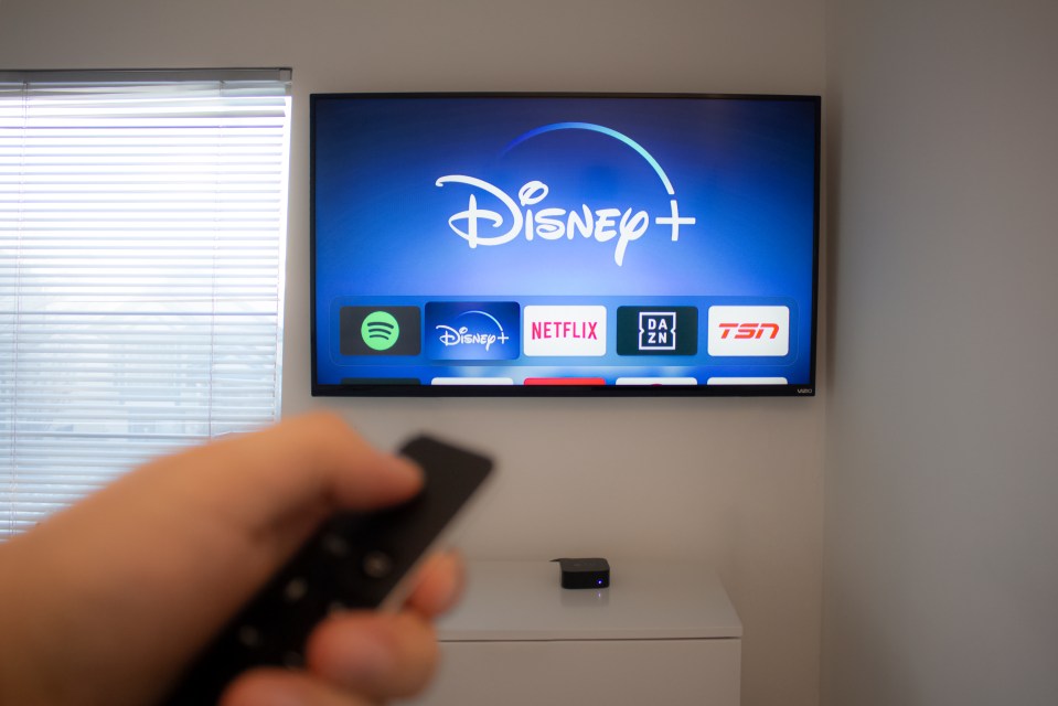 Person holding Apple TV remote, Disney+ app displayed on TV screen.