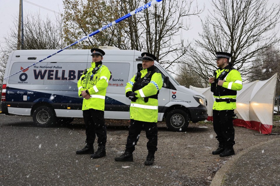 Three police officers standing outside a police van in the snow.