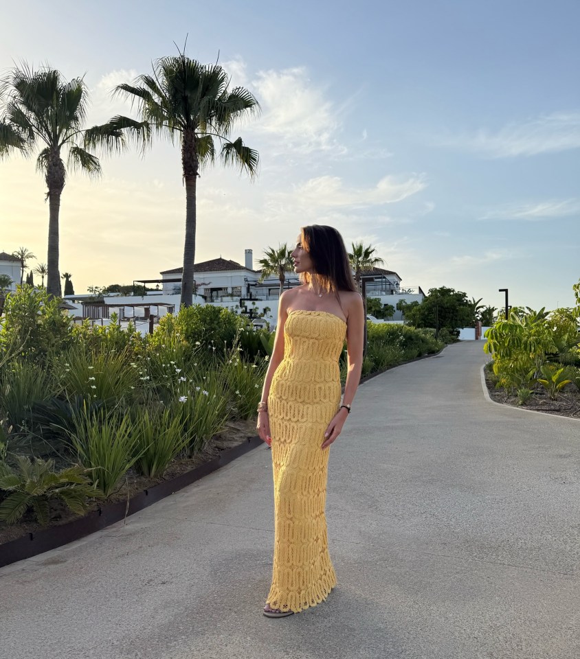 Woman in yellow crochet dress standing on a path.