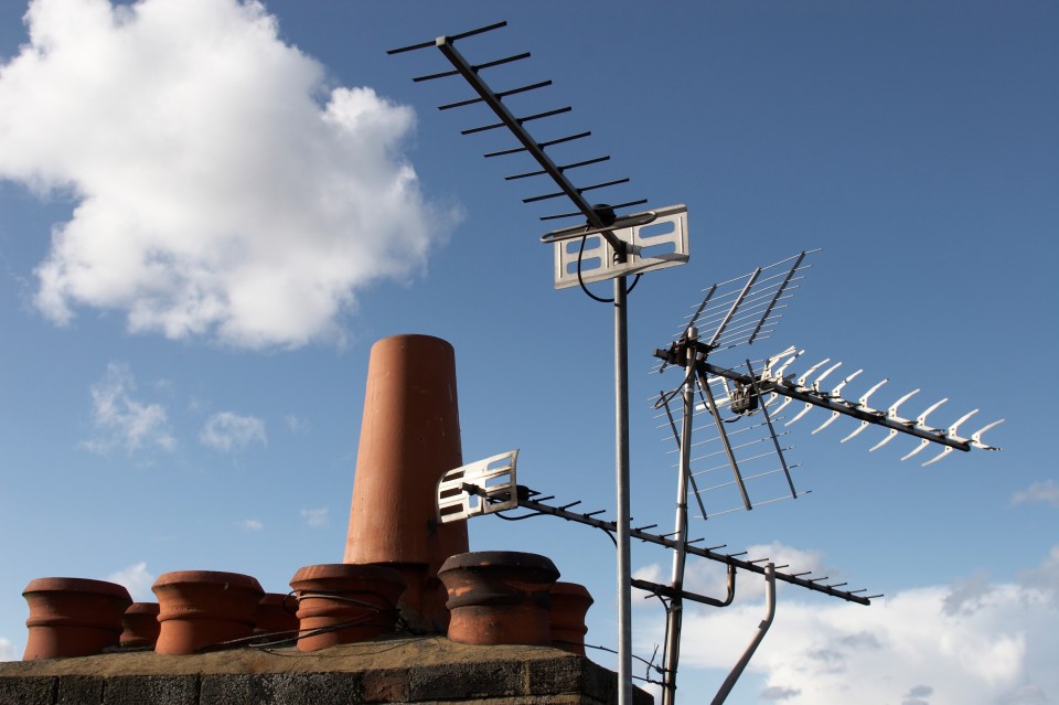 Television antennas on a rooftop against a blue sky.