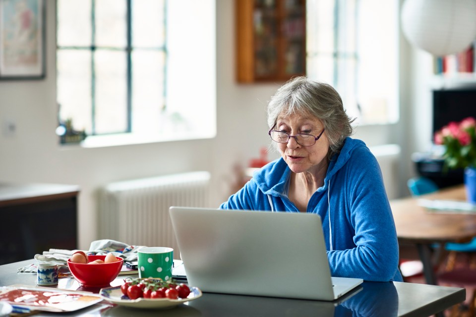 A woman in her 50s uses a laptop at home, concentrating on her work.