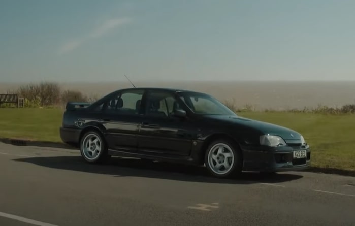Black Vauxhall Lotus Carlton driving on a road near the coast.