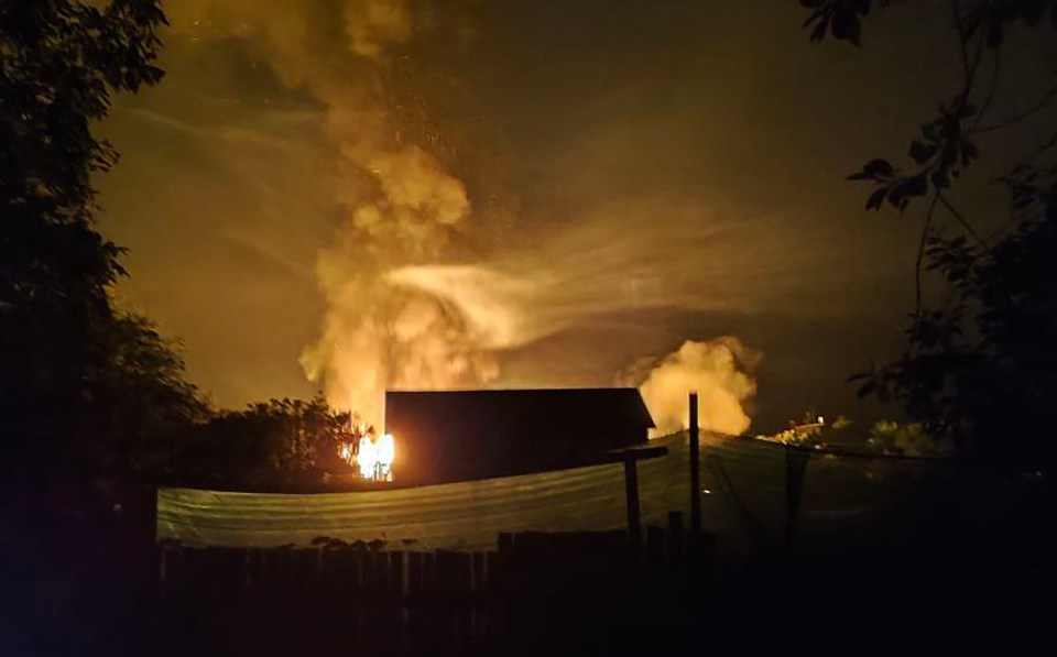 Nighttime view of a large fire burning near a building.