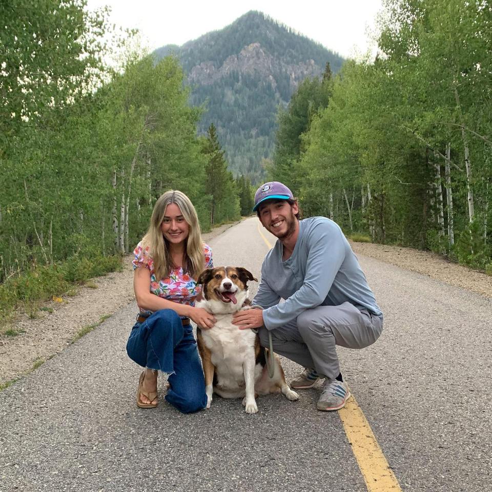 Couple and dog posing on a road in a mountainous area.