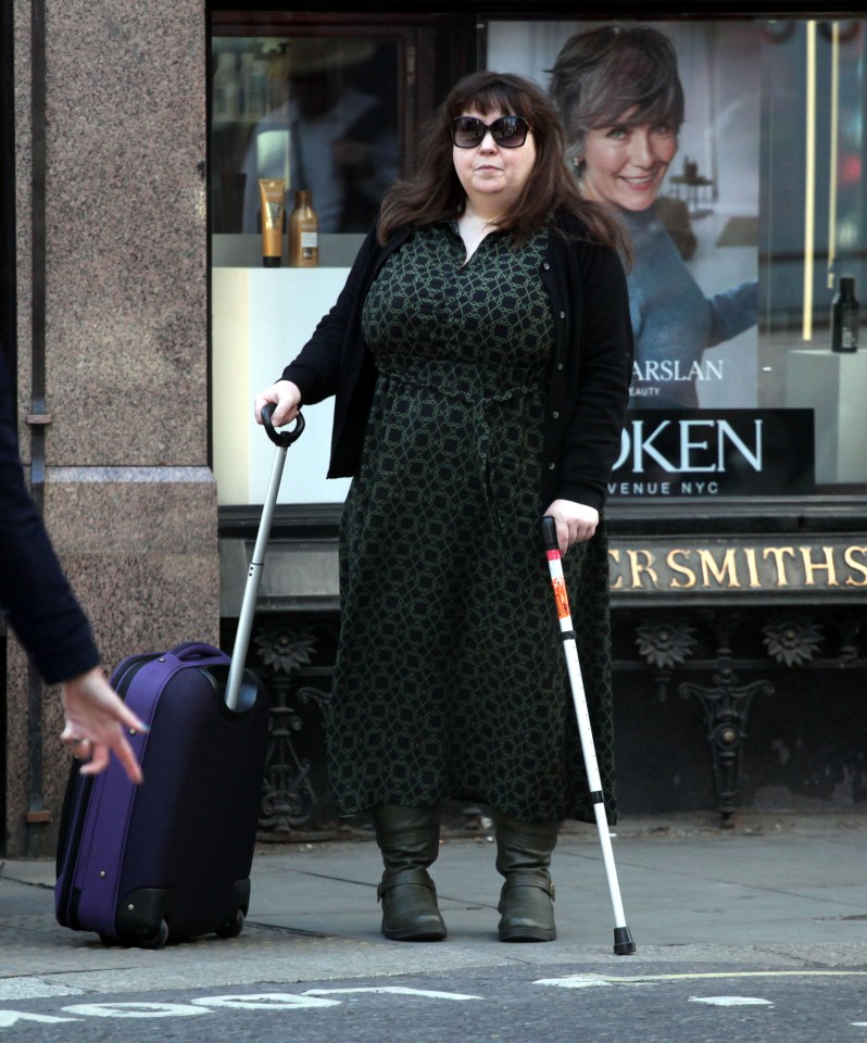 Woman with a cane and suitcase outside a London courthouse.