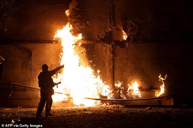 A firefighter stands by a fire and points to a hole following a drone strike in Kharkiv on June 5