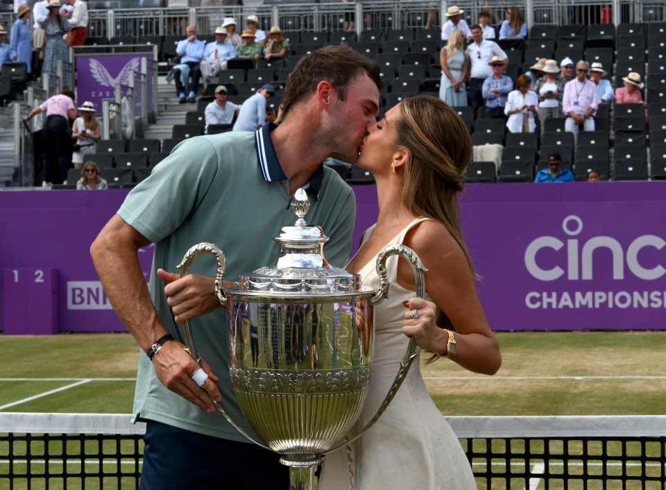 Tommy Paul kissing his girlfriend while holding a tennis trophy.