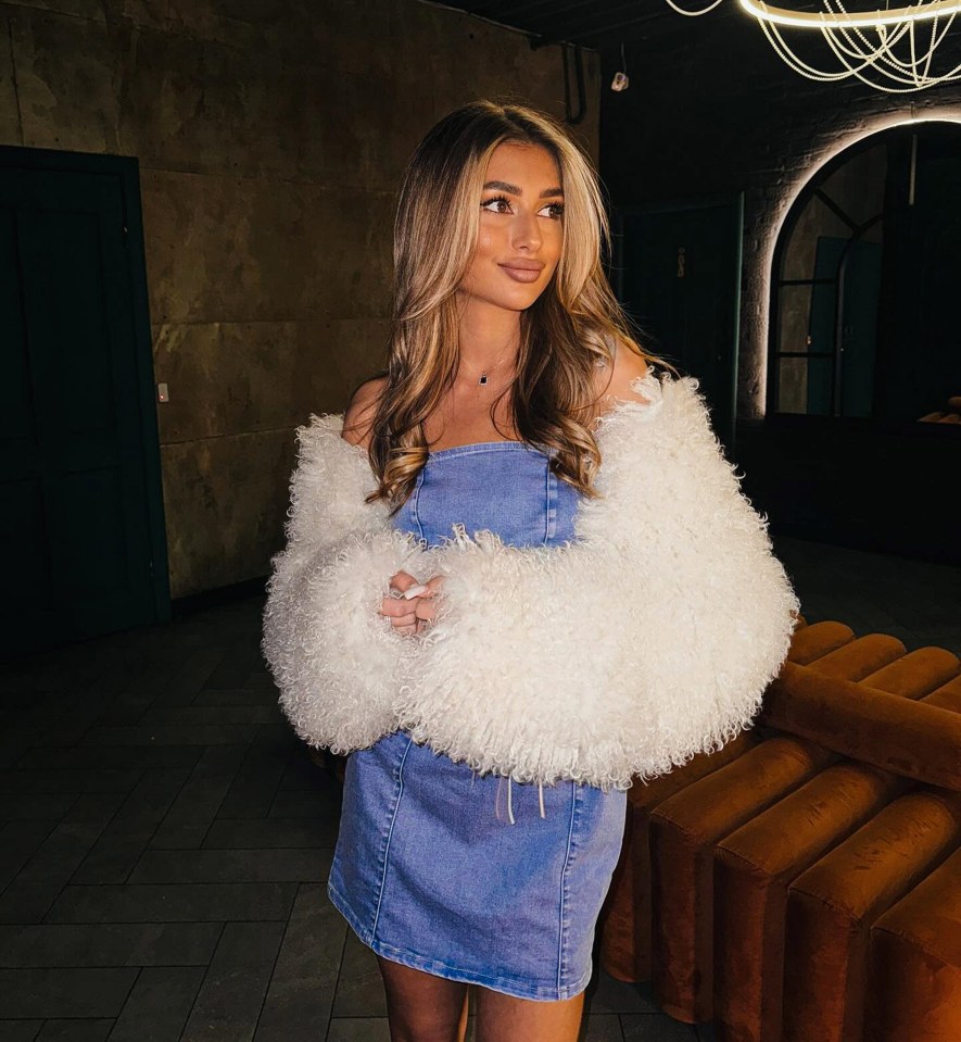 Woman in denim skirt and white fluffy jacket.